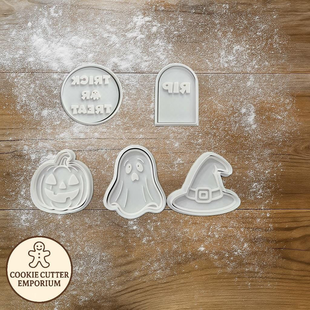 Set of Halloween-themed cookie cutters on a wooden surface with a rolling pin and checkered towel.