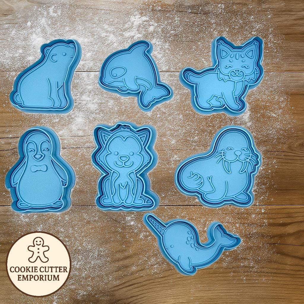 Set of blue animal-shaped cookie cutters on a wooden surface with a rolling pin and checkered towel.