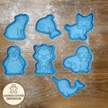 Set of blue animal-shaped cookie cutters on a wooden surface with a rolling pin and checkered towel.