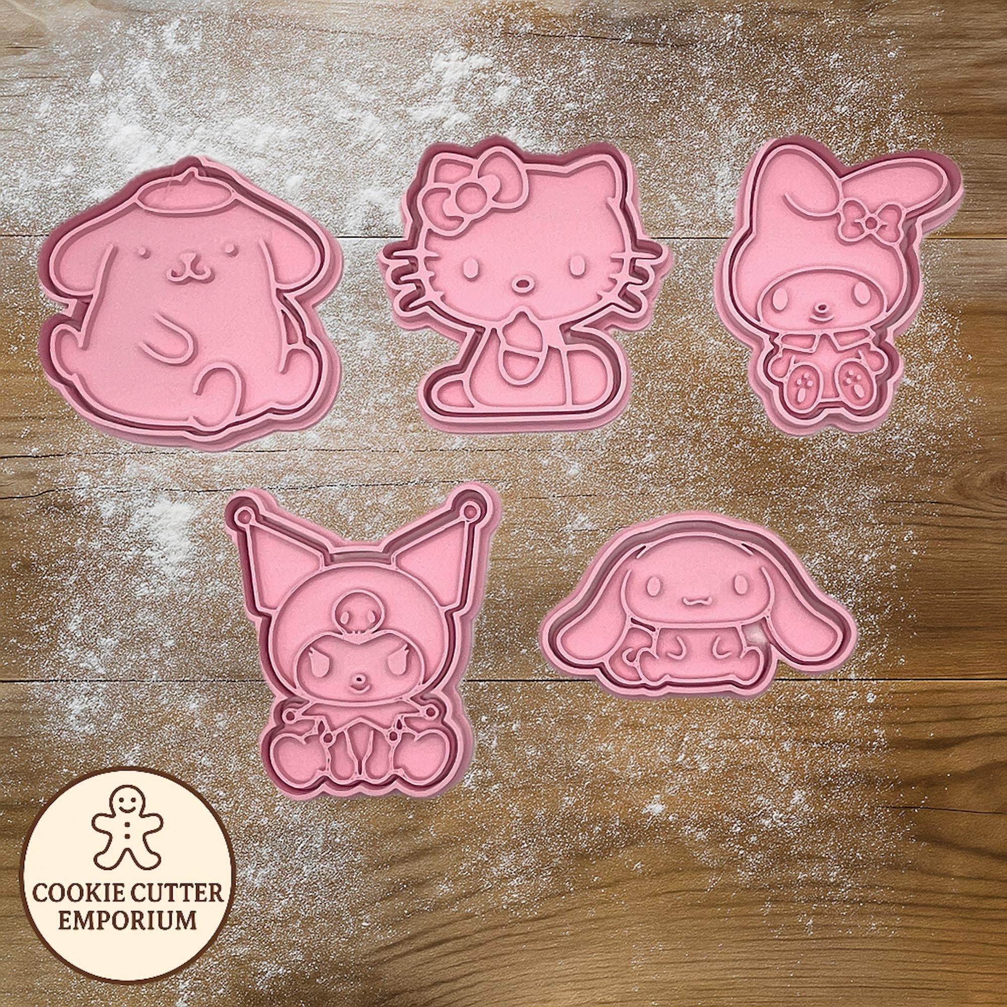 Set of pink cookie cutters shaped like cartoon characters on a wooden surface with a rolling pin and checkered cloth.