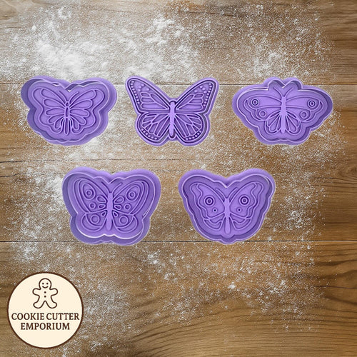 Butterfly-shaped cookie cutters on a wooden surface with a rolling pin and checkered towel.