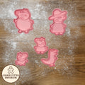 Pink cookie cutters shaped like cartoon characters on a wooden surface with a rolling pin and checkered towel.