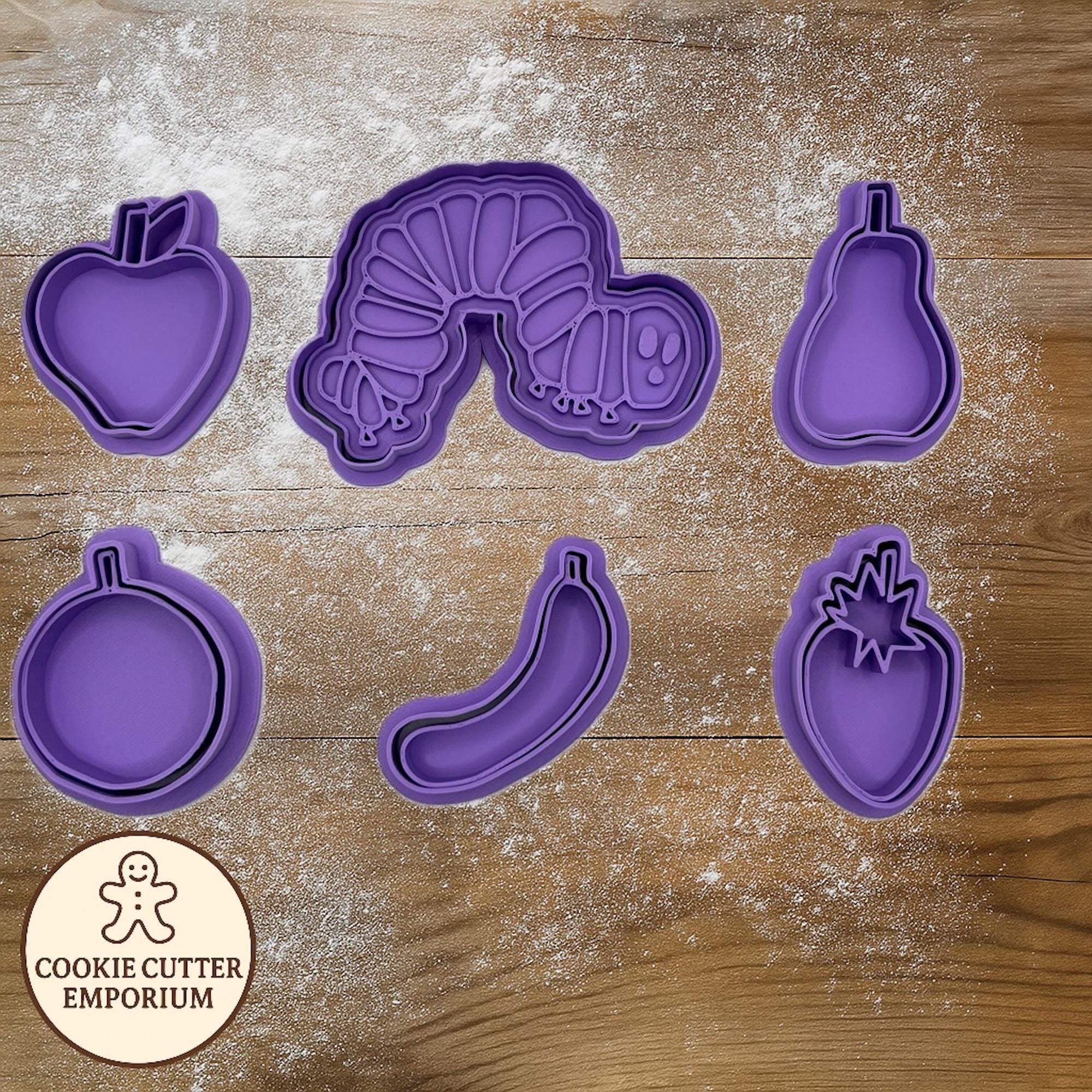 Set of purple cookie cutters on a wooden surface with a rolling pin and checkered towel.