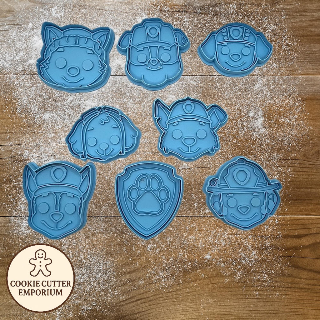 Set of blue cookie cutters shaped like dogs on a wooden surface with a rolling pin and checkered towel.