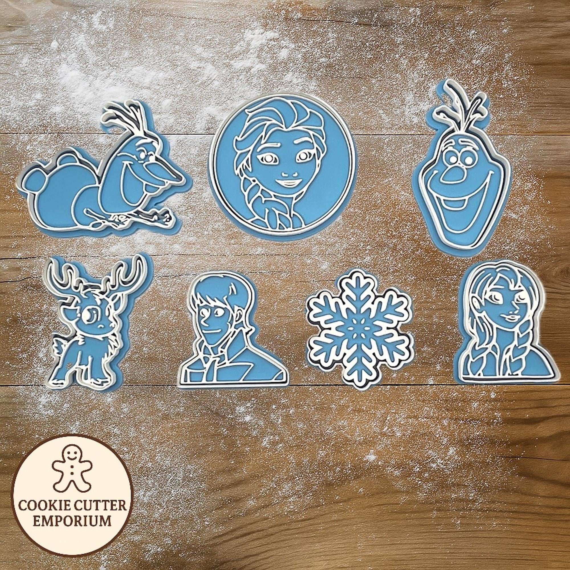 Cookie cutters shaped like characters from a popular animated movie on a wooden surface with a rolling pin and checkered towel.