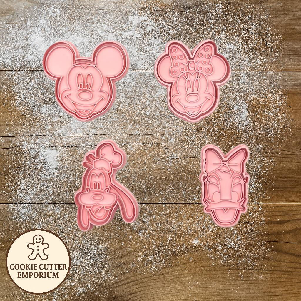 Pink cookie cutters shaped like cartoon characters on a wooden surface with a rolling pin and checkered towel.